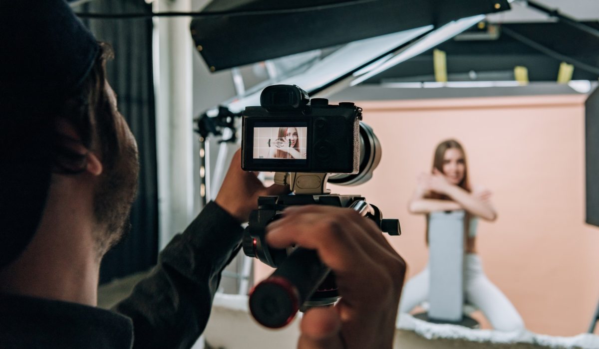 Over shoulder view of videographer filming beautiful model in photo studio